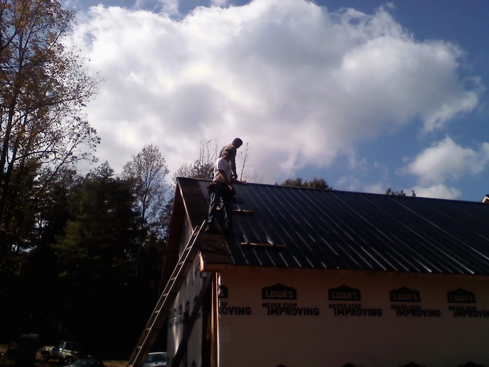 Roofer fastening dark metal panels high against a cloudy sky, from a Roof Inspection job in Manakin Sabot