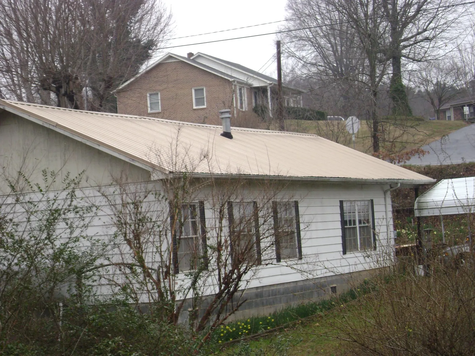 Tan metal roof on a white sided house set into a hillside — Commercial Roofing by Roofing Brothers in Manakin Sabot